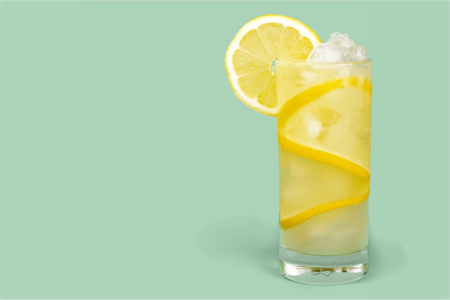 Hohes Glas Limonade mit Eis und einer Zitronenscheibe auf mintgrünem Hintergrund