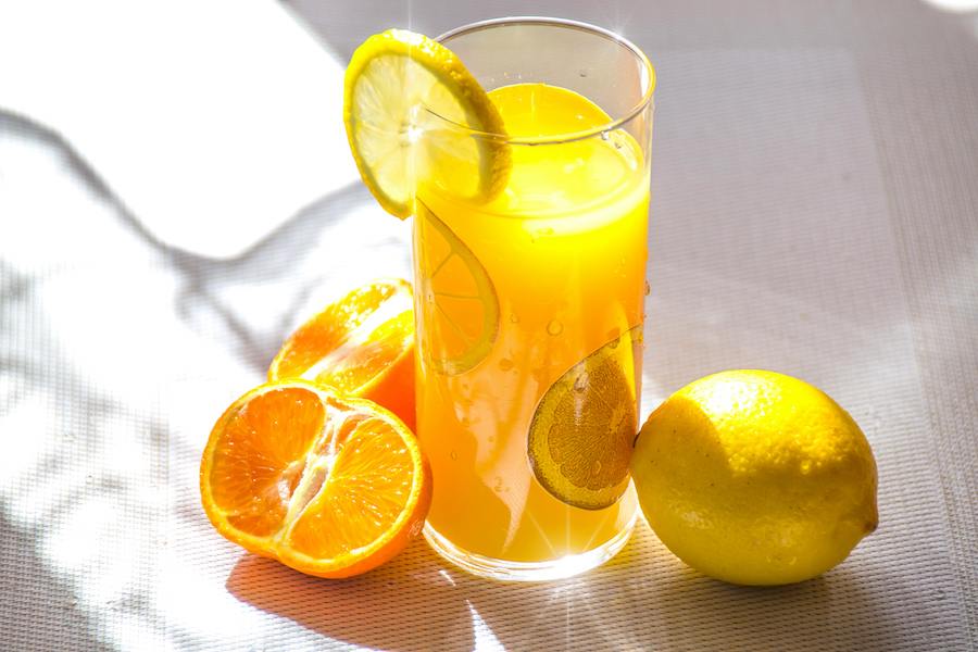 Glas Orangensaft im Sonnenlicht mit Zitronenscheiben, einer halbierten Mandarine und einer ganzen Zitrone