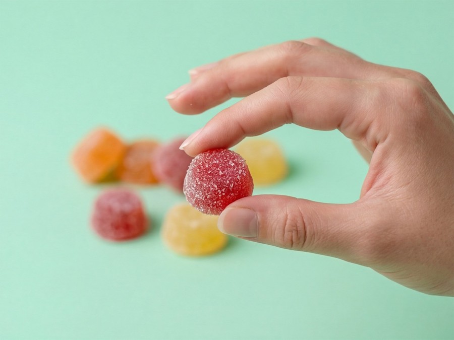 Hand hält ein gezuckertes rotes Fruchtgelee, weitere Gelees im Hintergrund auf mintgrüner Fläche