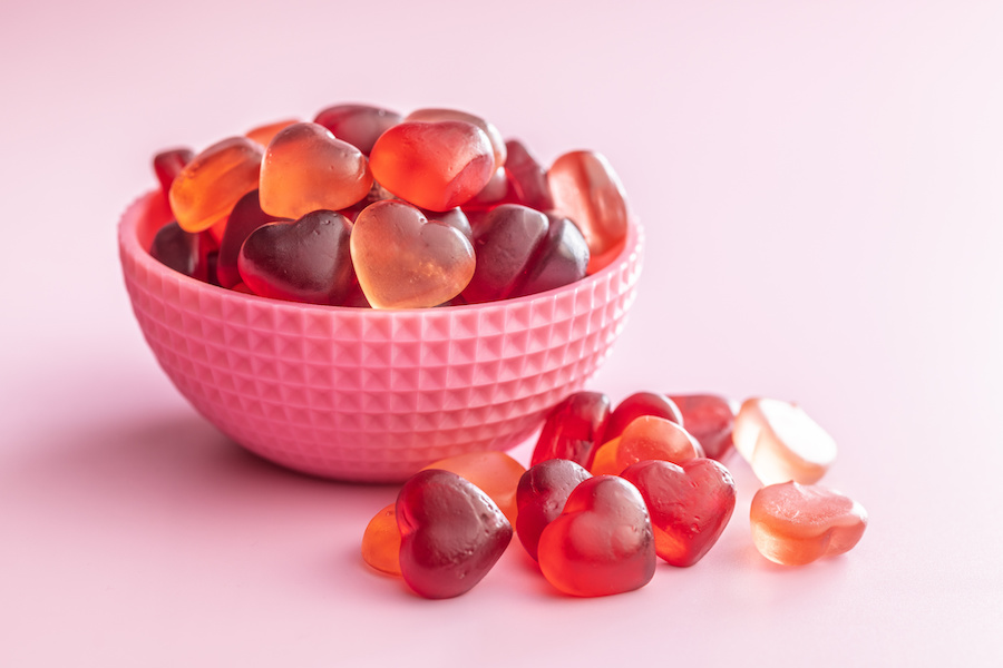 Rosa Schale mit roten und orangen herzförmigen Fruchtgummis auf rosa Hintergrund