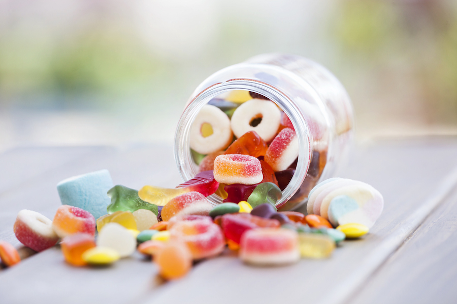 Bunte Fruchtgummis fallen aus einem umgekippten Glas auf einem Holztisch
