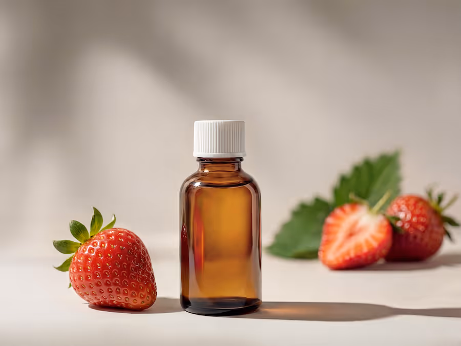Kleine braune Glasflasche mit weißem Verschluss neben frischen Erdbeeren und einem Blatt