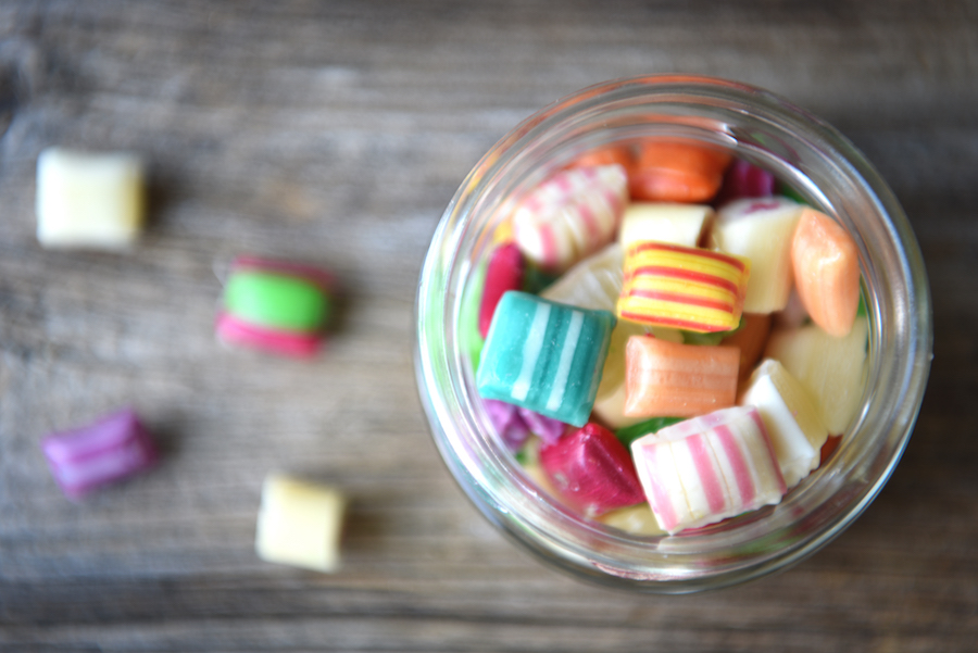 Glas mit bunten gestreiften Bonbons auf einem Holztisch von oben