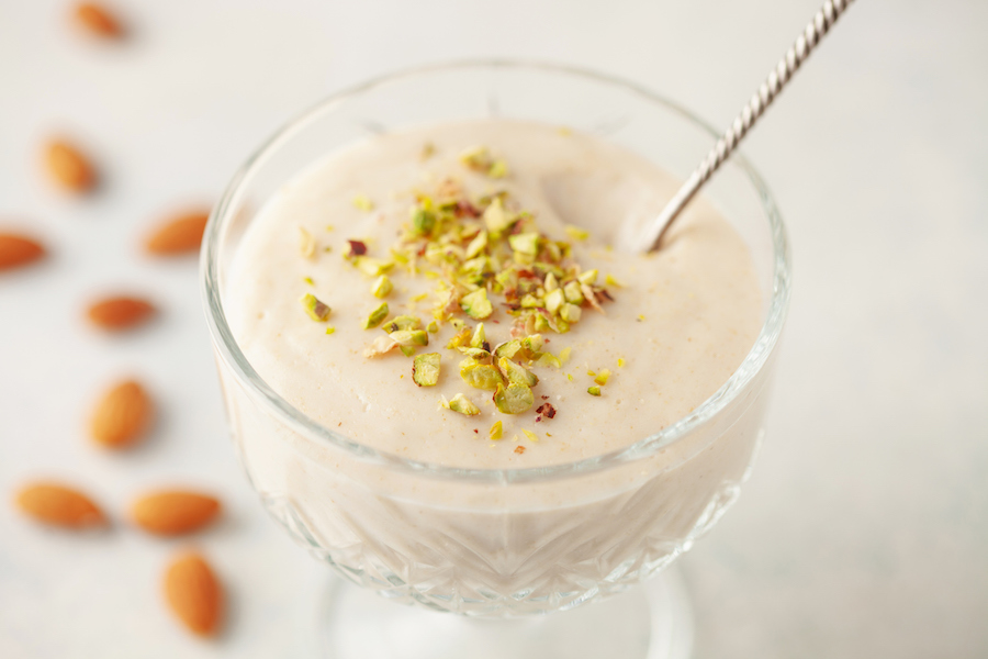Glasschale mit cremigem Pudding und gehackten Pistazien, daneben verstreute Mandeln