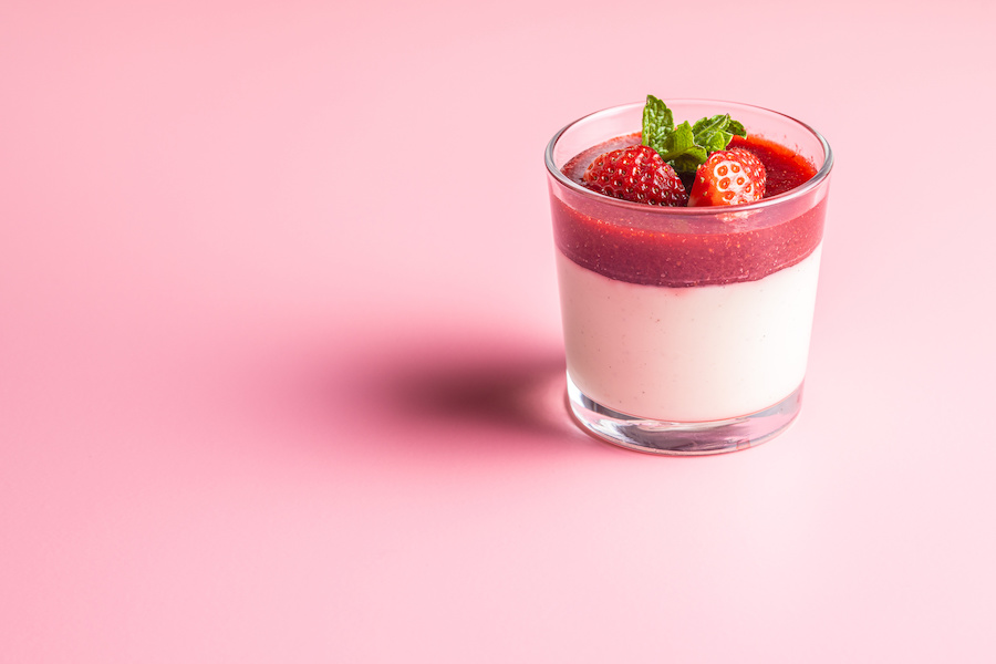Glas Panna Cotta mit Erdbeersauce, frischen Erdbeeren und Minze vor rosa Hintergrund