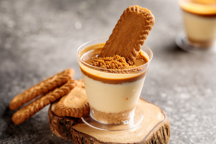 Geschichtetes Karamell-Keks-Dessert im Glas mit einem Gewürzkeks obenauf, serviert auf einem Holzbrett