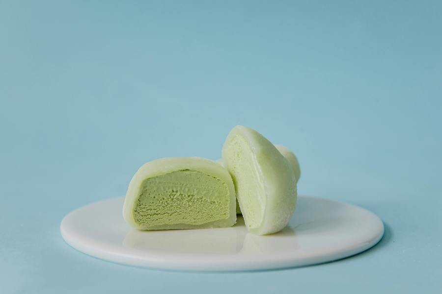 Halbiertes Grüntee-Mochi-Eis auf einem weißen Teller vor hellblauem Hintergrund
