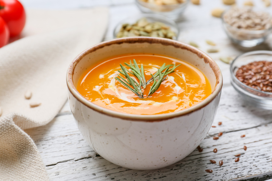 Schale cremige Kürbissuppe mit Rosmarin, umgeben von Samen und Tomaten