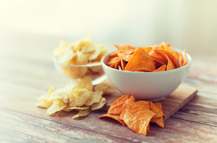 Schalen mit orangen Tortilla-Chips und Kartoffelchips auf einem rustikalen Holztisch
