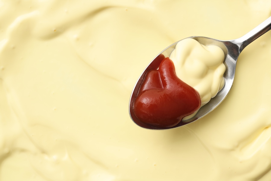 Löffel mit Ketchup und Mayonnaise auf einer glatten Mayonnaise-Oberfläche