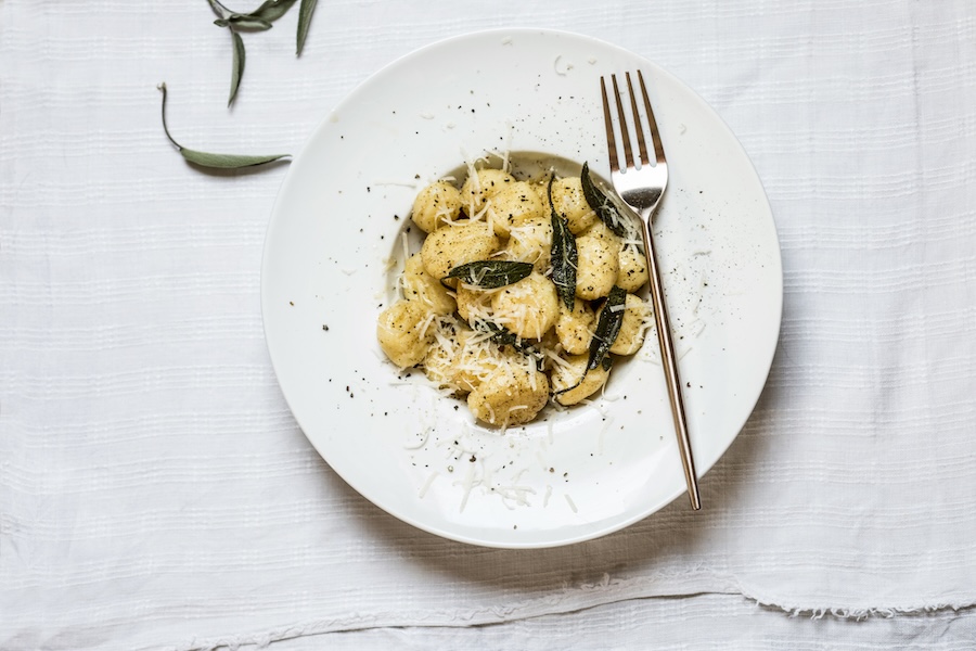 Weißer Teller mit Gnocchi, geriebenem Käse, Salbeiblättern und schwarzem Pfeffer, daneben eine Gabel