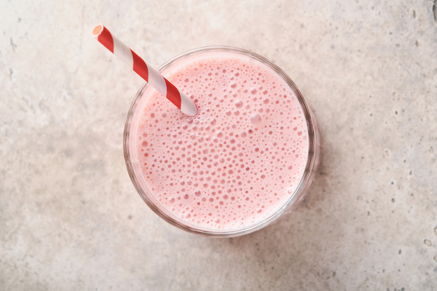 Glas schaumiger rosa Erdbeerdrink mit rot gestreiftem Trinkhalm, von oben