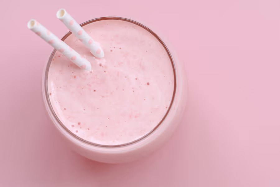 Glas rosa Erdbeer-Milchshake mit zwei Papiertrinkhalmen vor rosa Hintergrund, von oben