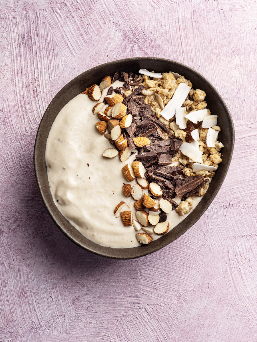 Schale mit cremigem Porridge, Mandeln, dunklen Schokostücken und Kokoschips, von oben