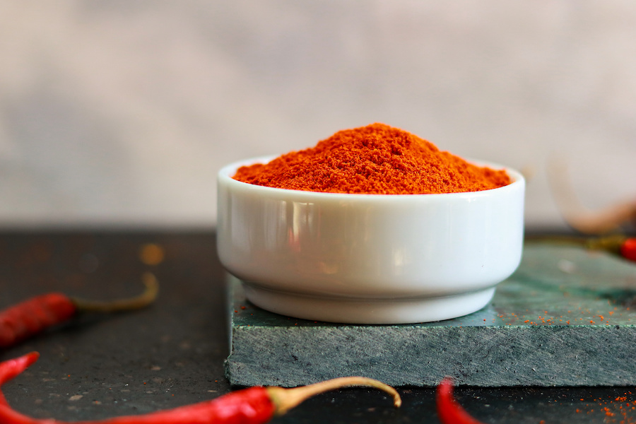 Weiße Schale mit rotem Paprikapulver auf einer Schieferplatte mit getrockneten Chilischoten