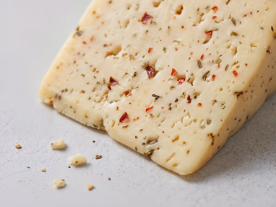 Nahaufnahme eines Käsestücks mit Kräutern und Chiliflocken