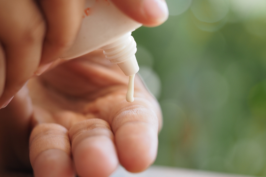 Nahaufnahme von Lotion, die aus einer Tube auf eine Fingerspitze gedrückt wird
