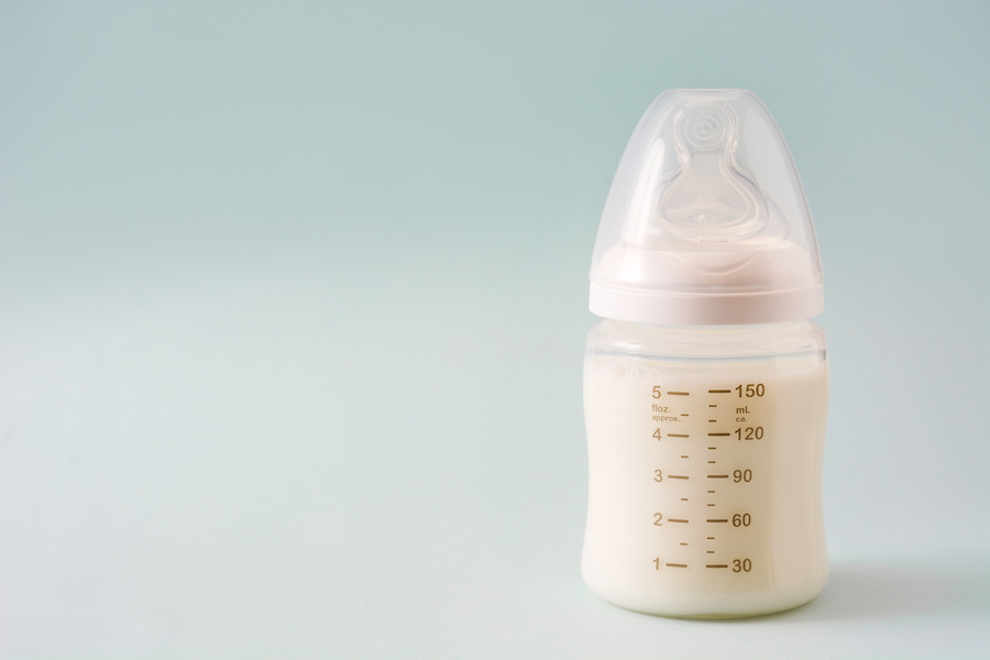Babyflasche mit angerührter Säuglingsmilch vor hellblauem Hintergrund