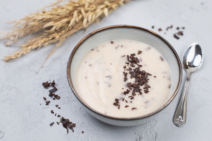 Schale cremiger Vanillepudding mit dunklen Schokoflocken neben getrockneten Haferähren