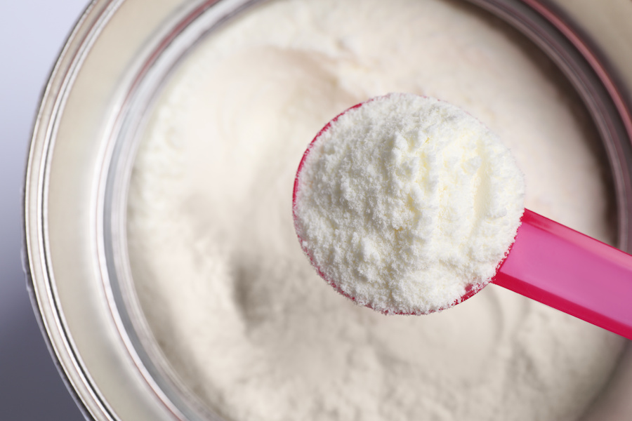 Rosa Messlöffel mit Milchpulver über einer geöffneten Dose Säuglingsmilch