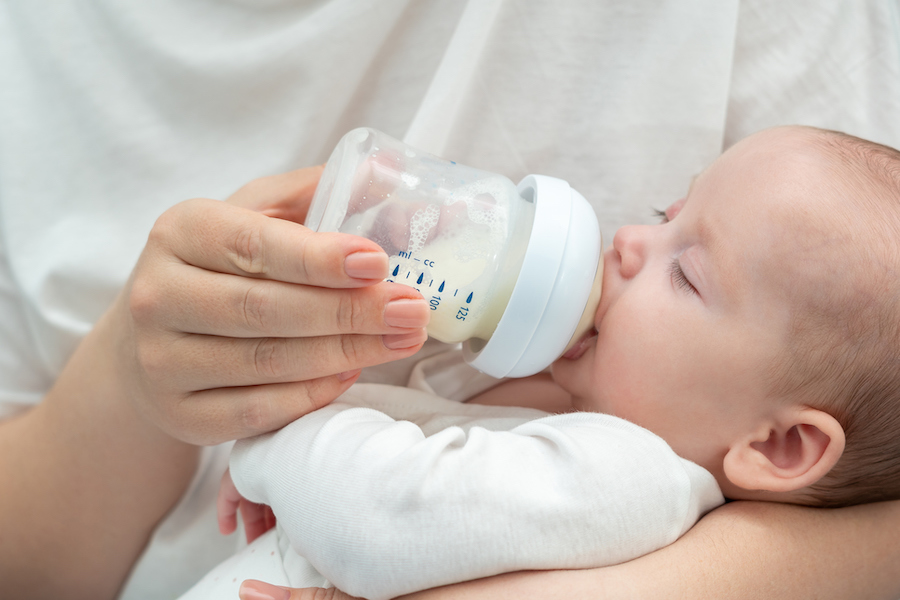 Baby wird in den Armen eines Elternteils mit dem Fläschchen gefüttert