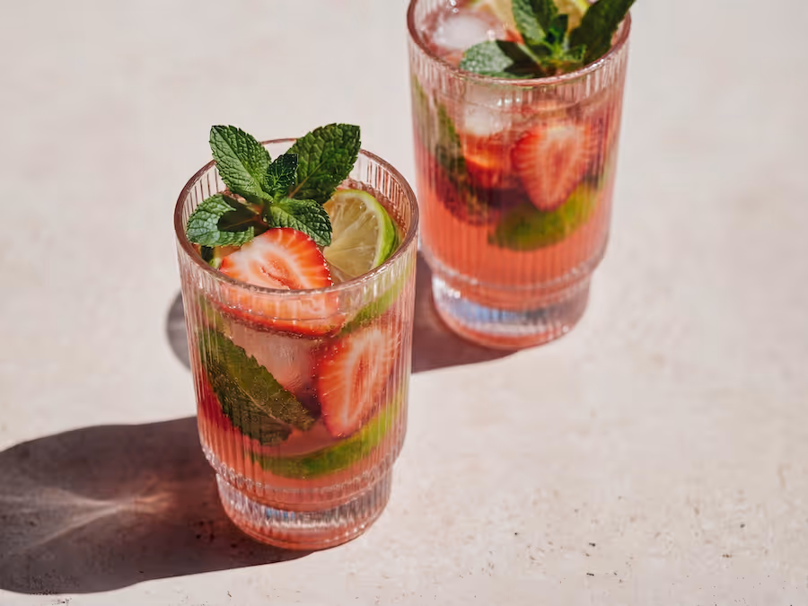 Zwei Rillengläser mit Erdbeerdrink, Minze, Limette und Eis auf einem Steintisch