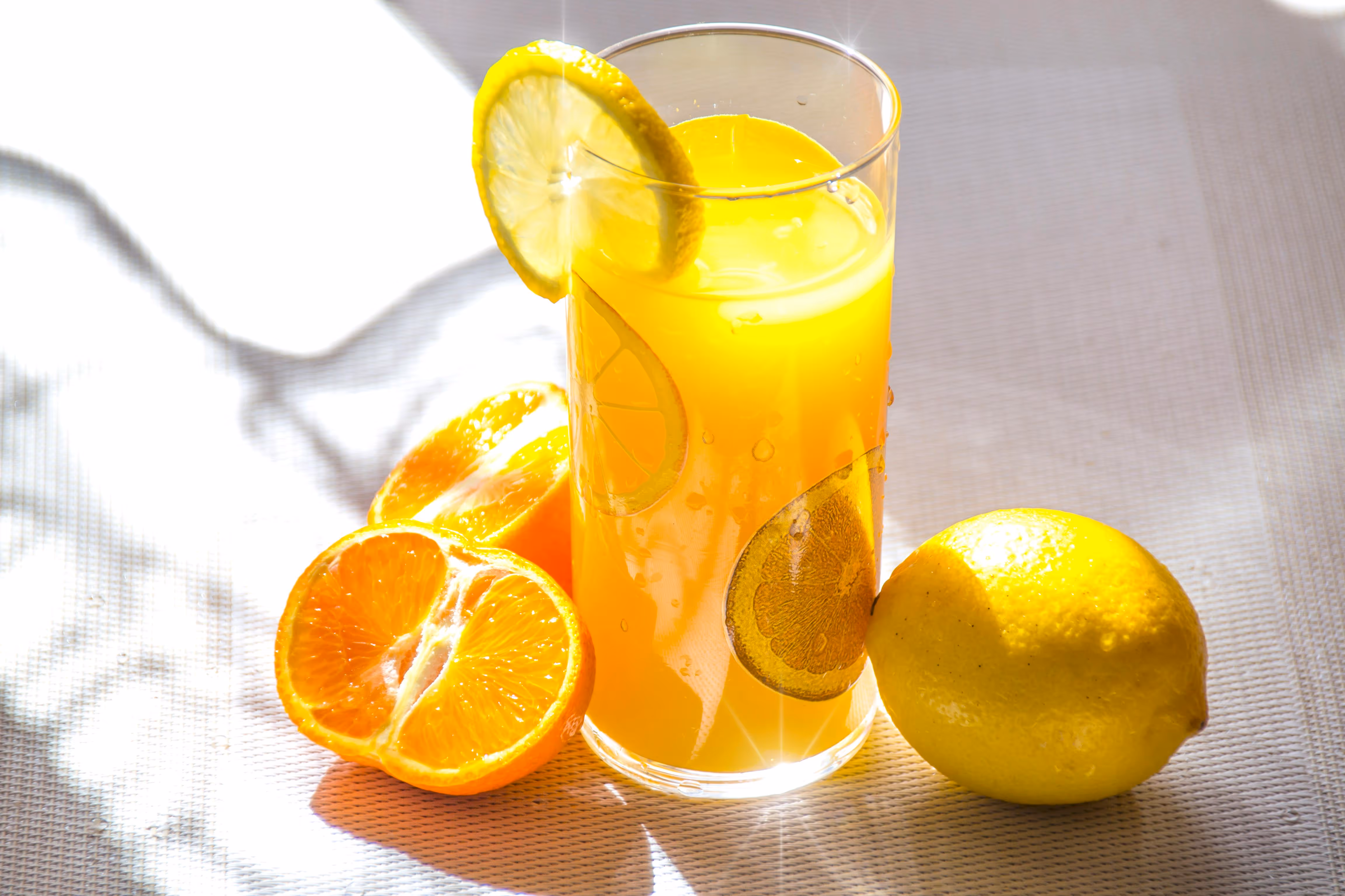 Glas Orangensaft mit Zitrusscheiben, halbierten Orangen und einer Zitrone im Sonnenlicht