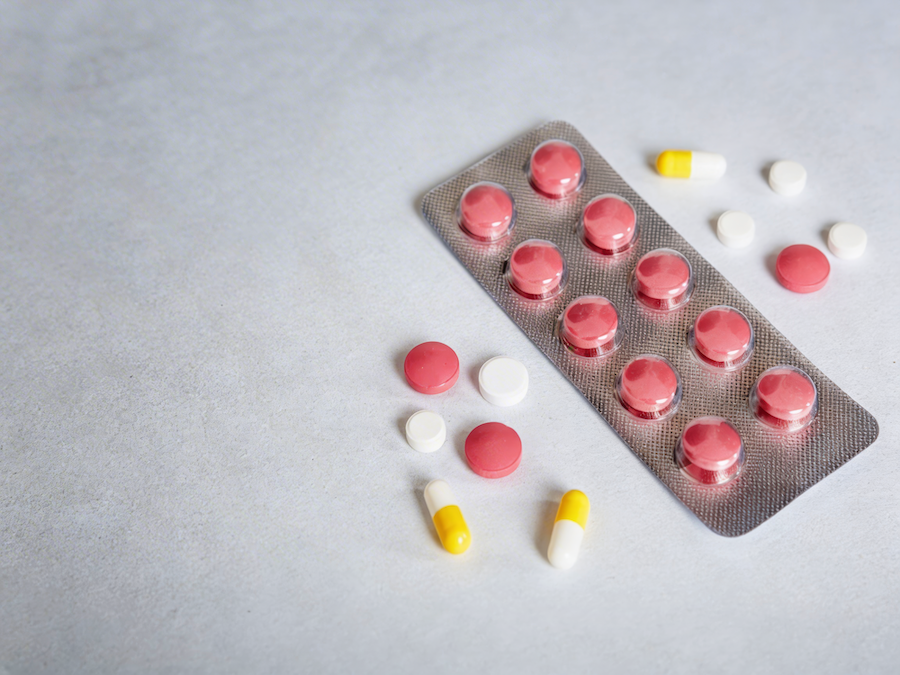 Blisterpackung mit roten Tabletten und losen weißen, roten und gelben Pillen auf hellgrauer Fläche