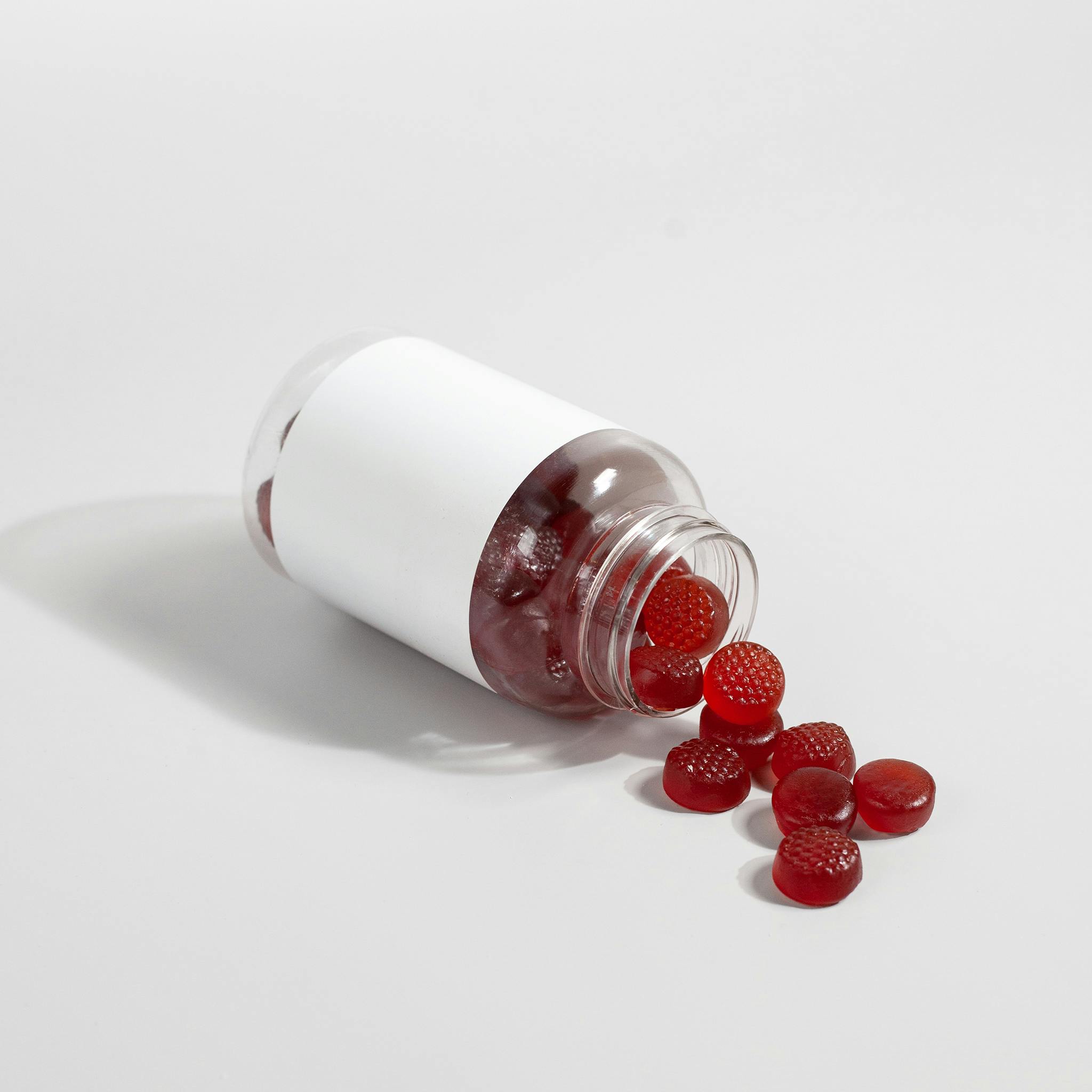 Rote Nahrungsergänzungs-Gummis fallen aus einer umgekippten weißen Dose