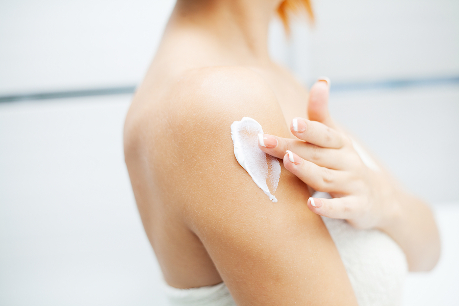 Frau trägt einen Streifen Lotion auf ihre Schulter auf