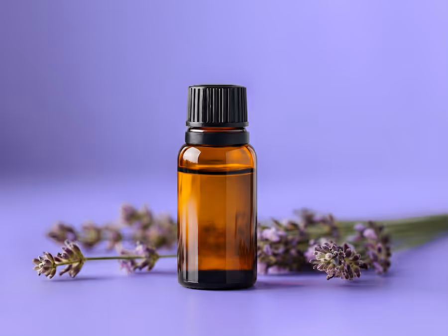Kleine Braunglasflasche mit Lavendelaroma und Lavendelzweigen auf violettem Hintergrund