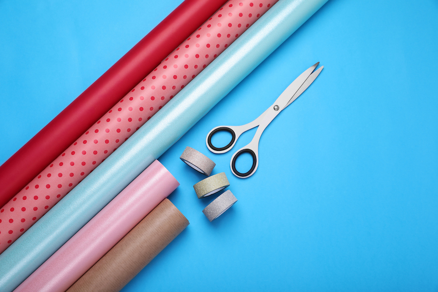 Fünf Rollen Geschenkpapier in verschiedenen Farben und Mustern neben Schere und Klebeband