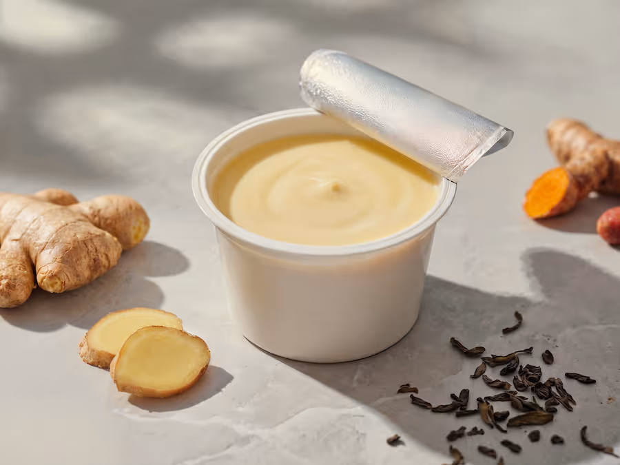 Opened cup of creamy yogurt alternative next to fresh ginger, turmeric root and loose tea leaves