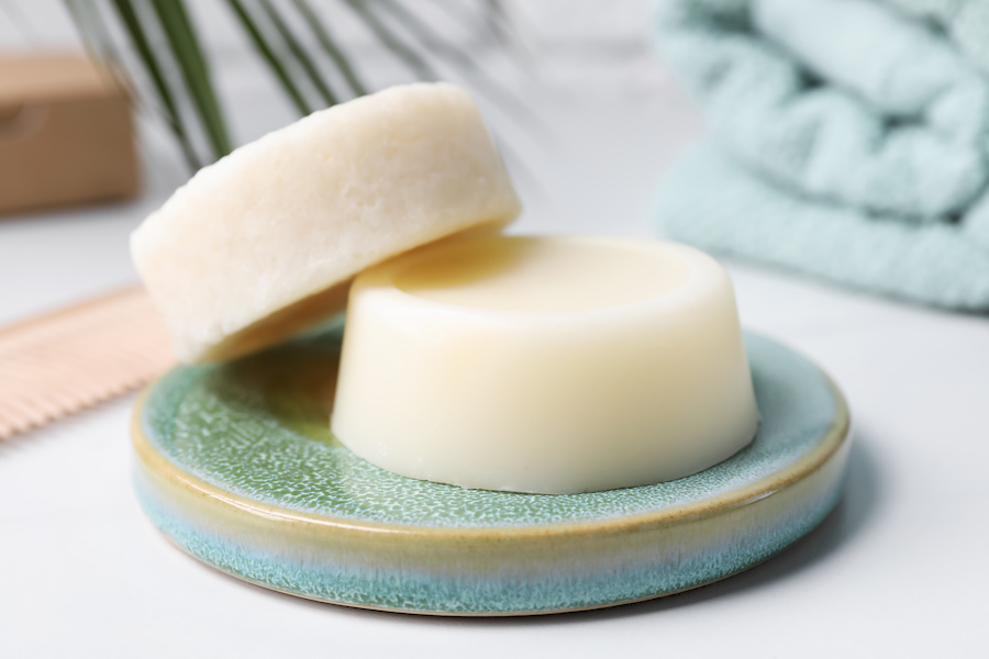 Zwei feste Shampoo-Stücke auf einem türkisen Keramikteller neben Holzkamm und gefalteten Handtüchern
