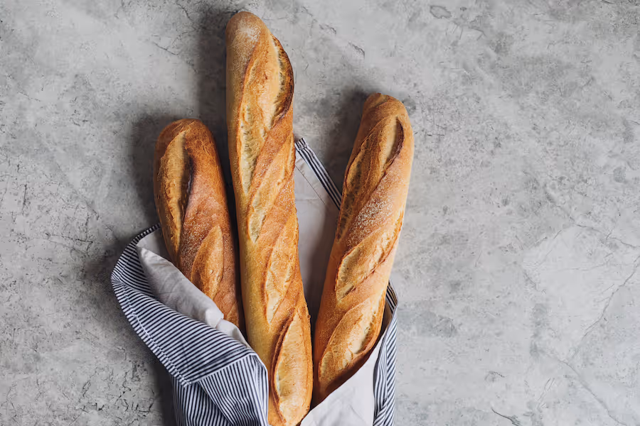 Drei knusprige Baguettes in einem gestreiften Tuch auf grauer Steinfläche