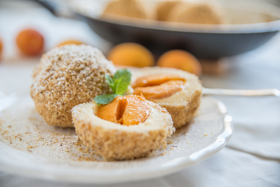 Marillenknödel in Bröseln, einer aufgeschnitten, mit Minze auf einem weißen Teller