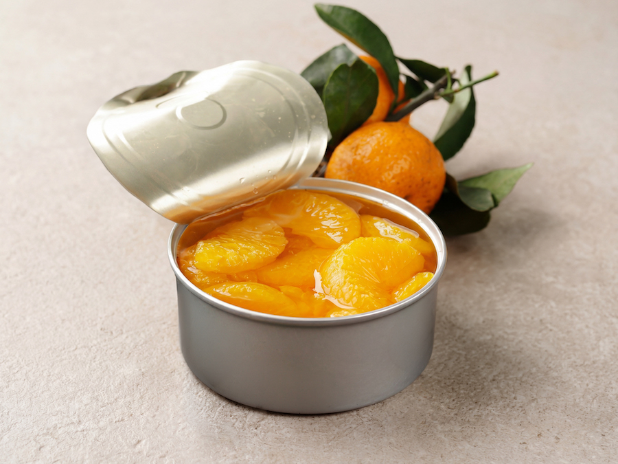 Geöffnete Dose Mandarinenspalten in Sirup, dahinter eine frische Mandarine mit Blättern