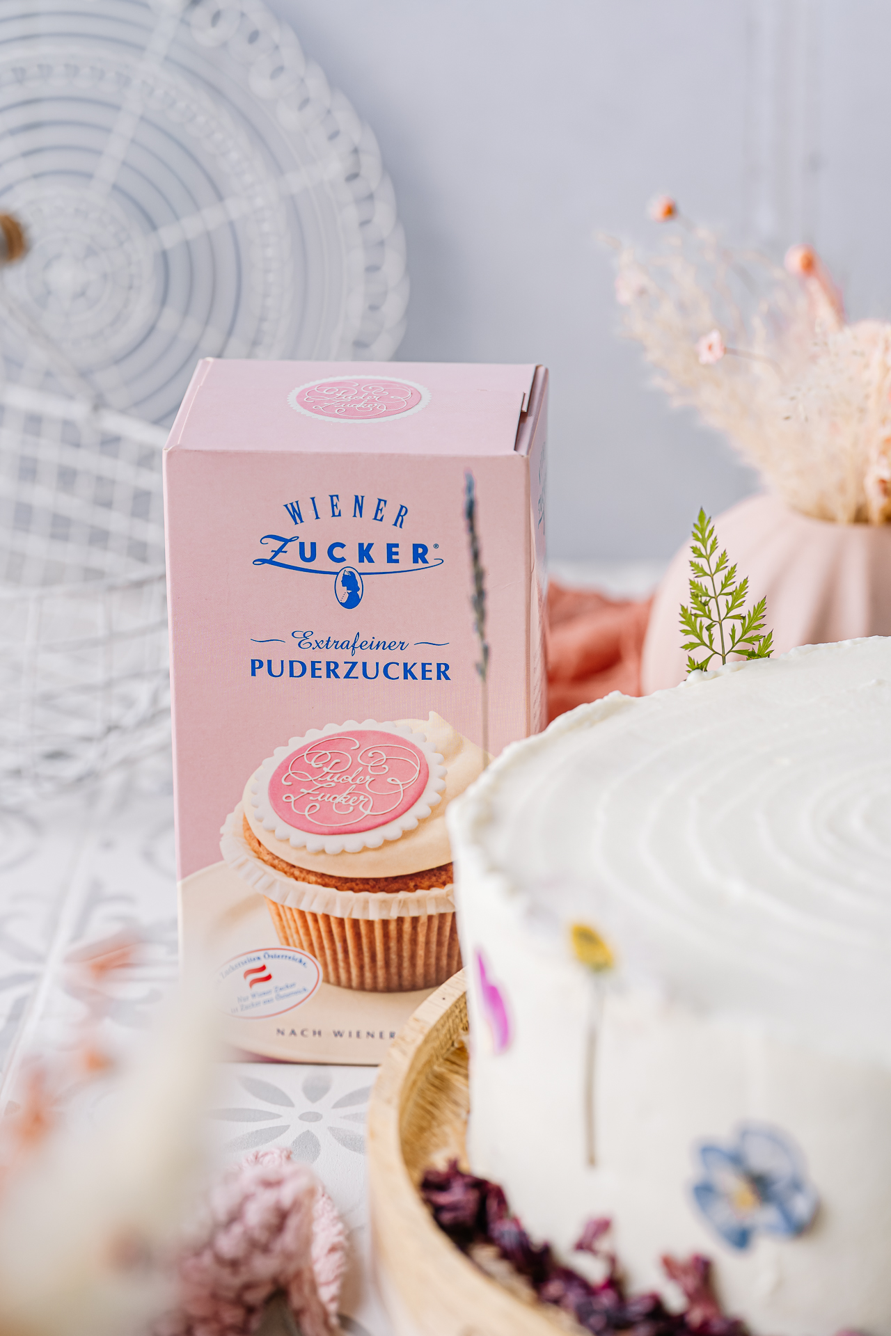 Packung Wiener Zucker Extrafeiner Puderzucker neben einer weißen Torte mit essbaren Blüten [no AI]