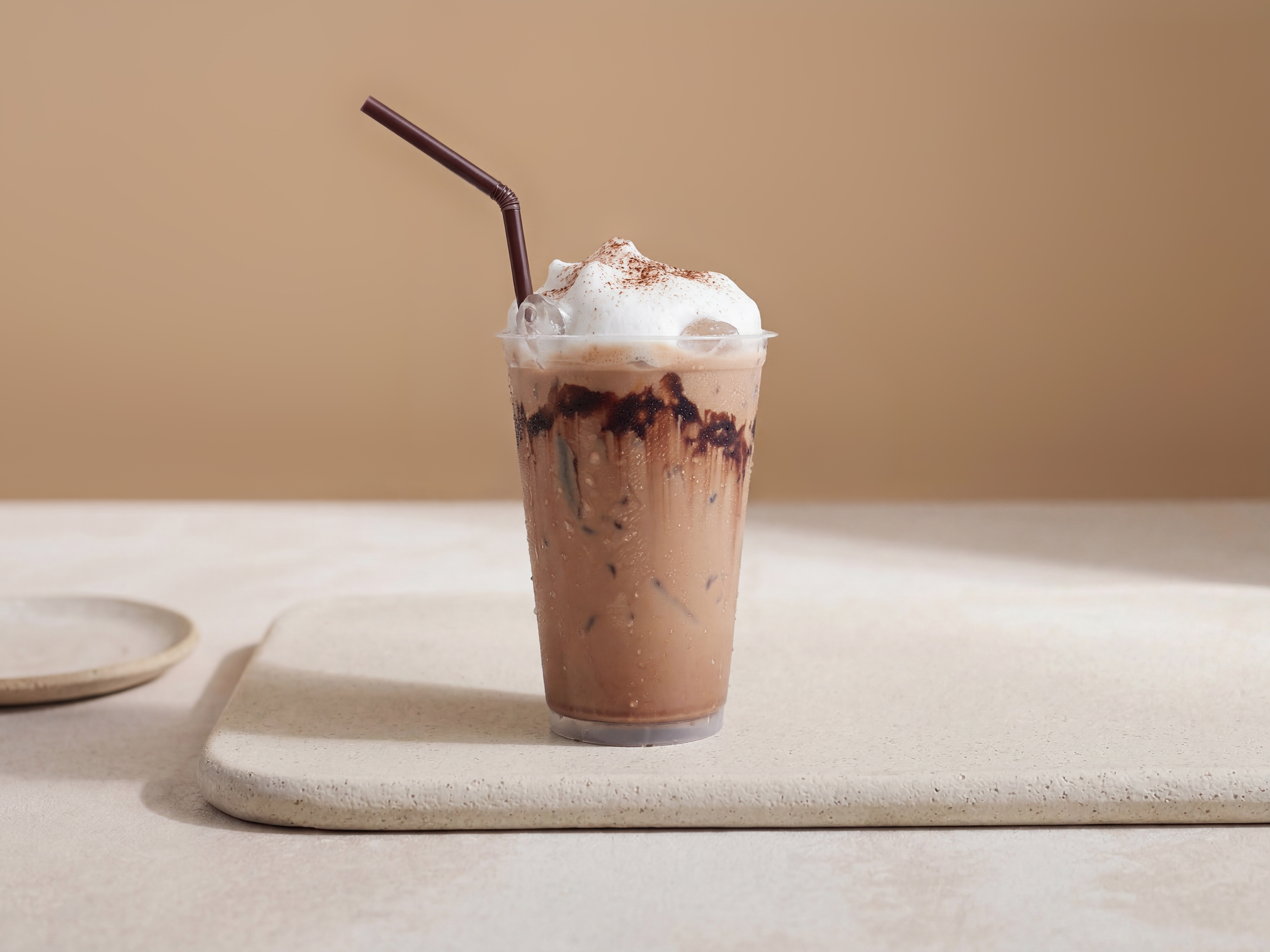 Schokoladen-Frappé mit Eis im Plastikbecher, garniert mit Schlagobers und Kakao