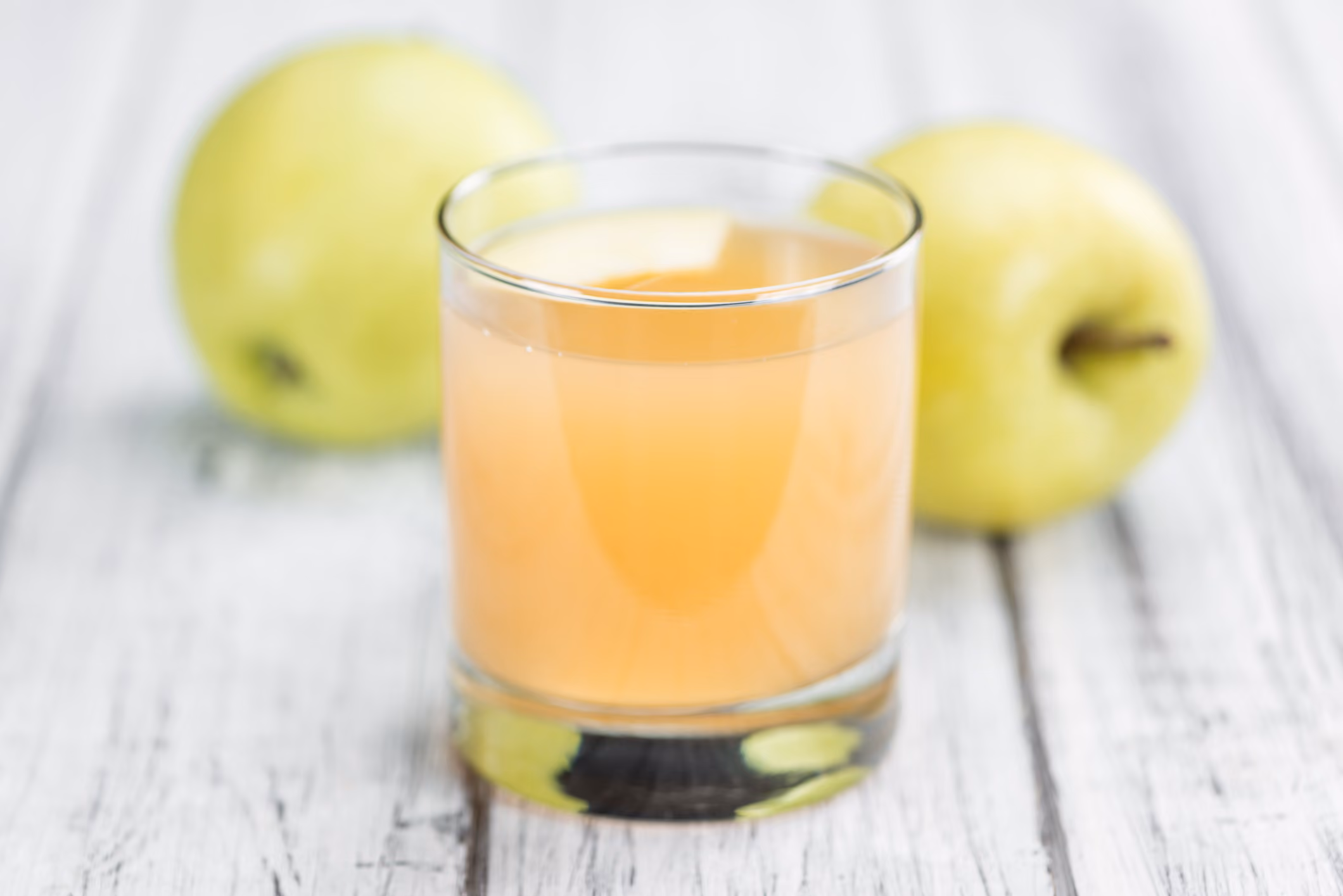Glas naturtrüber Apfelsaft mit zwei grünen Äpfeln auf einem weißen Holztisch