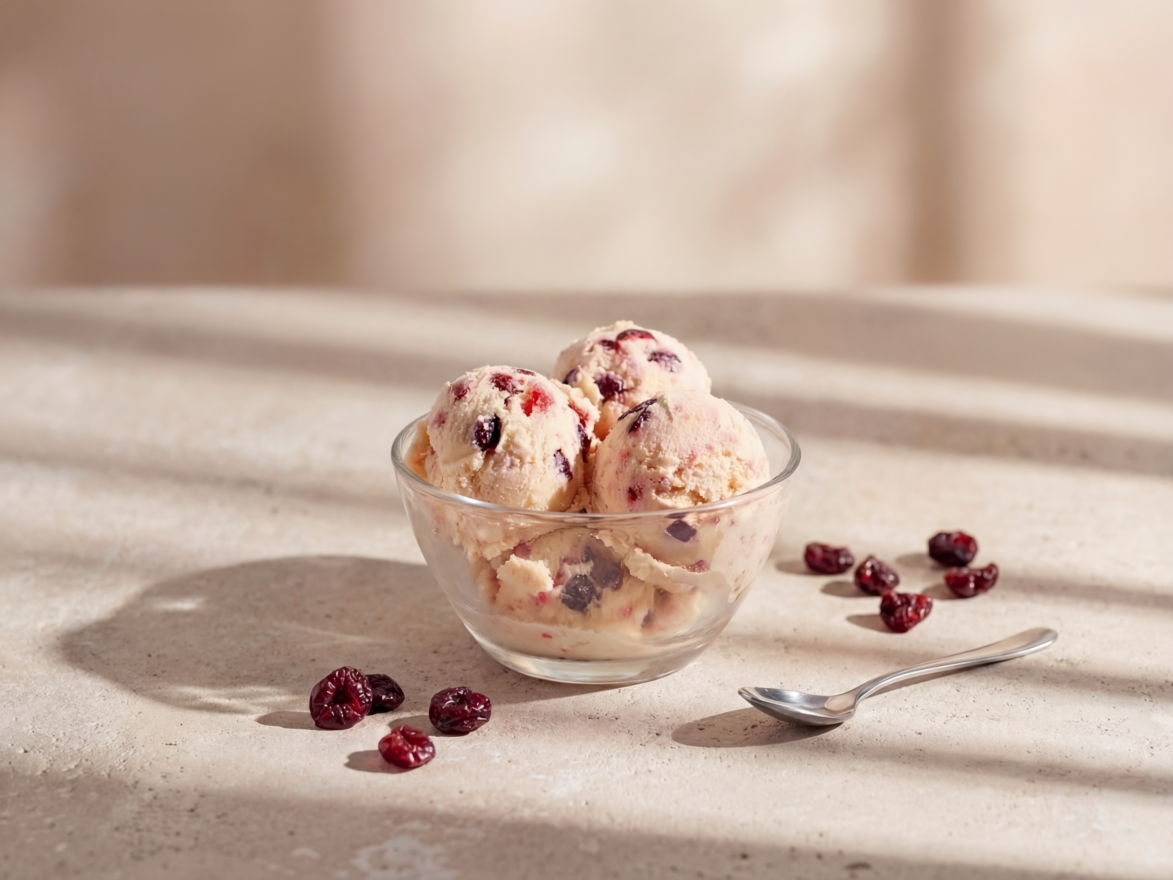 Glasschale Vanilleeis mit getrockneten Cranberrys, daneben verstreute Cranberrys und ein Löffel