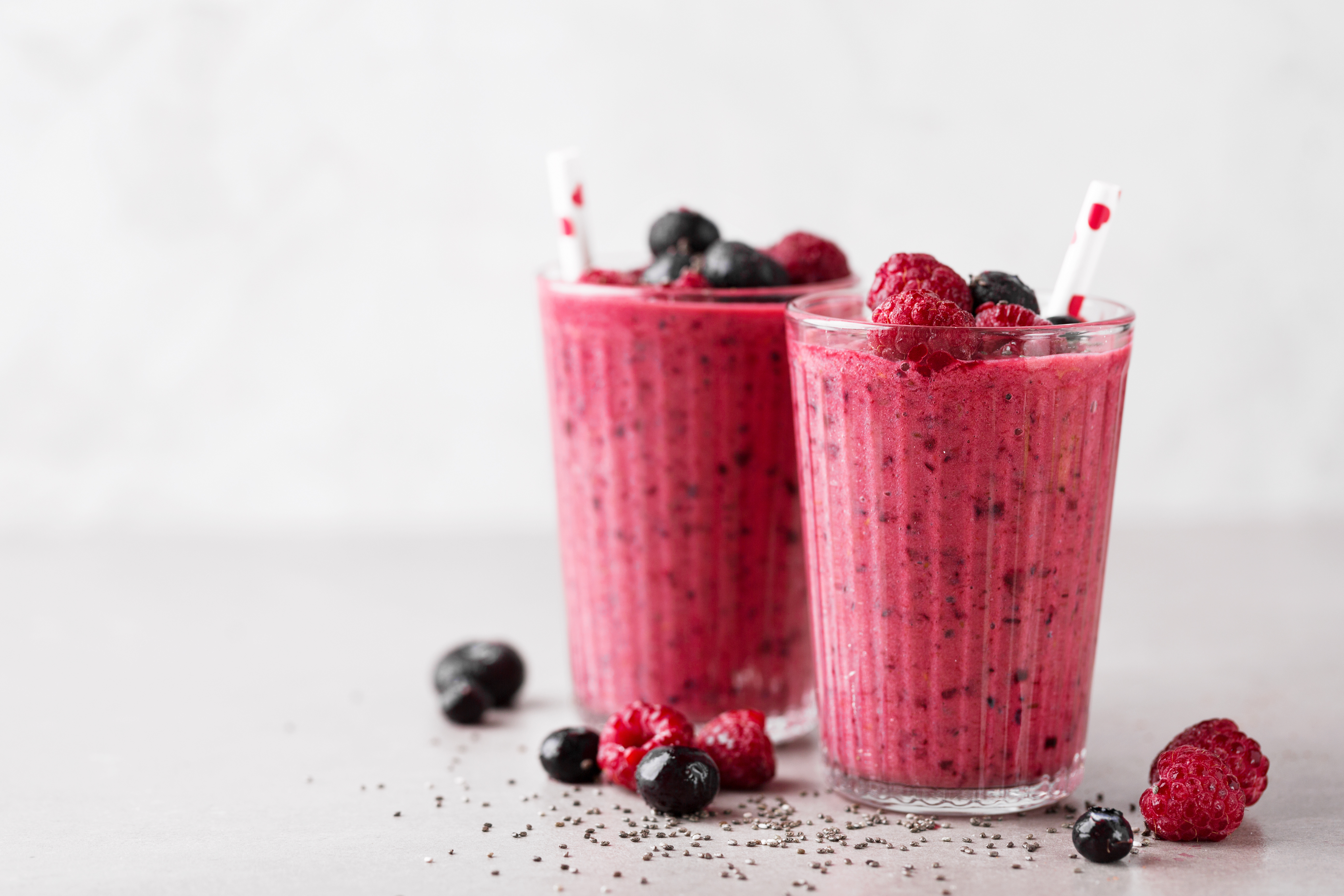 Zwei Gläser Beeren-Smoothie mit Strohhalmen, Himbeeren und Johannisbeeren auf dem Tisch
