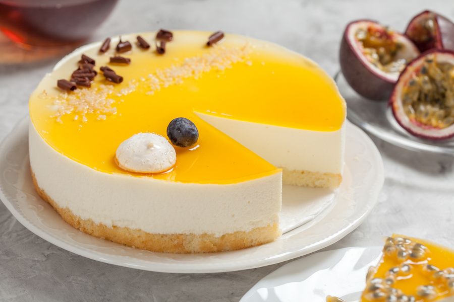Käsetorte mit Passionsfruchtglasur, ein Stück angeschnitten, daneben halbierte Passionsfrüchte