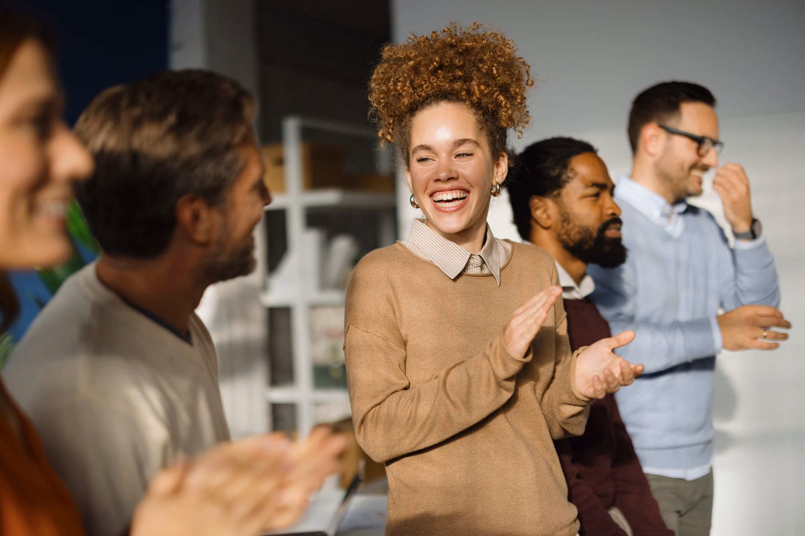 Gruppe junger Kolleginnen und Kollegen lacht und applaudiert in einem Büro [no AI]