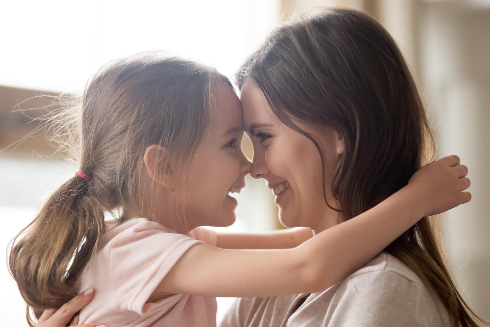 Mutter und kleine Tochter lachen sich Stirn an Stirn in einer Umarmung an