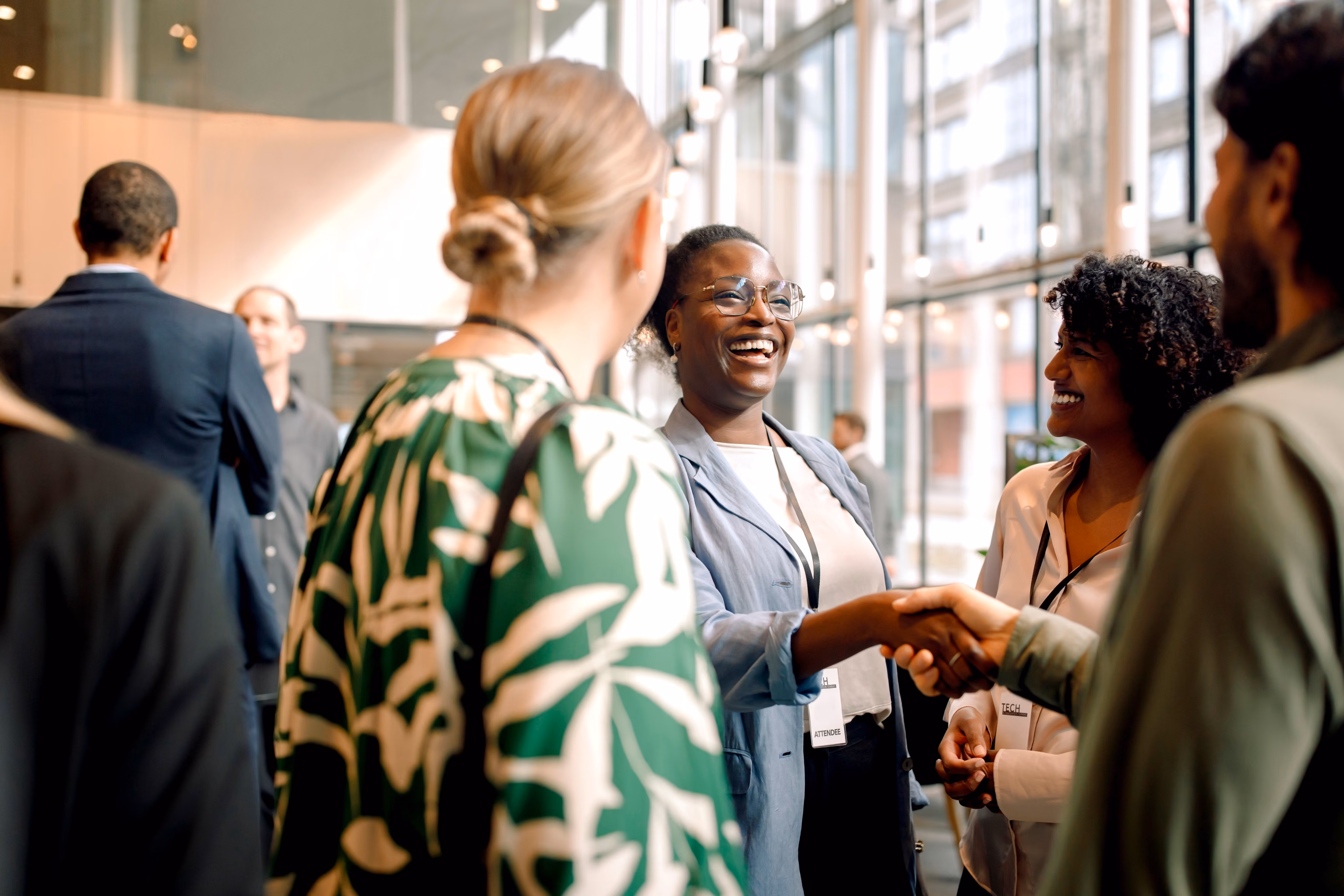 Professionals with name badges greeting each other and shaking hands at a networking event [no AI]