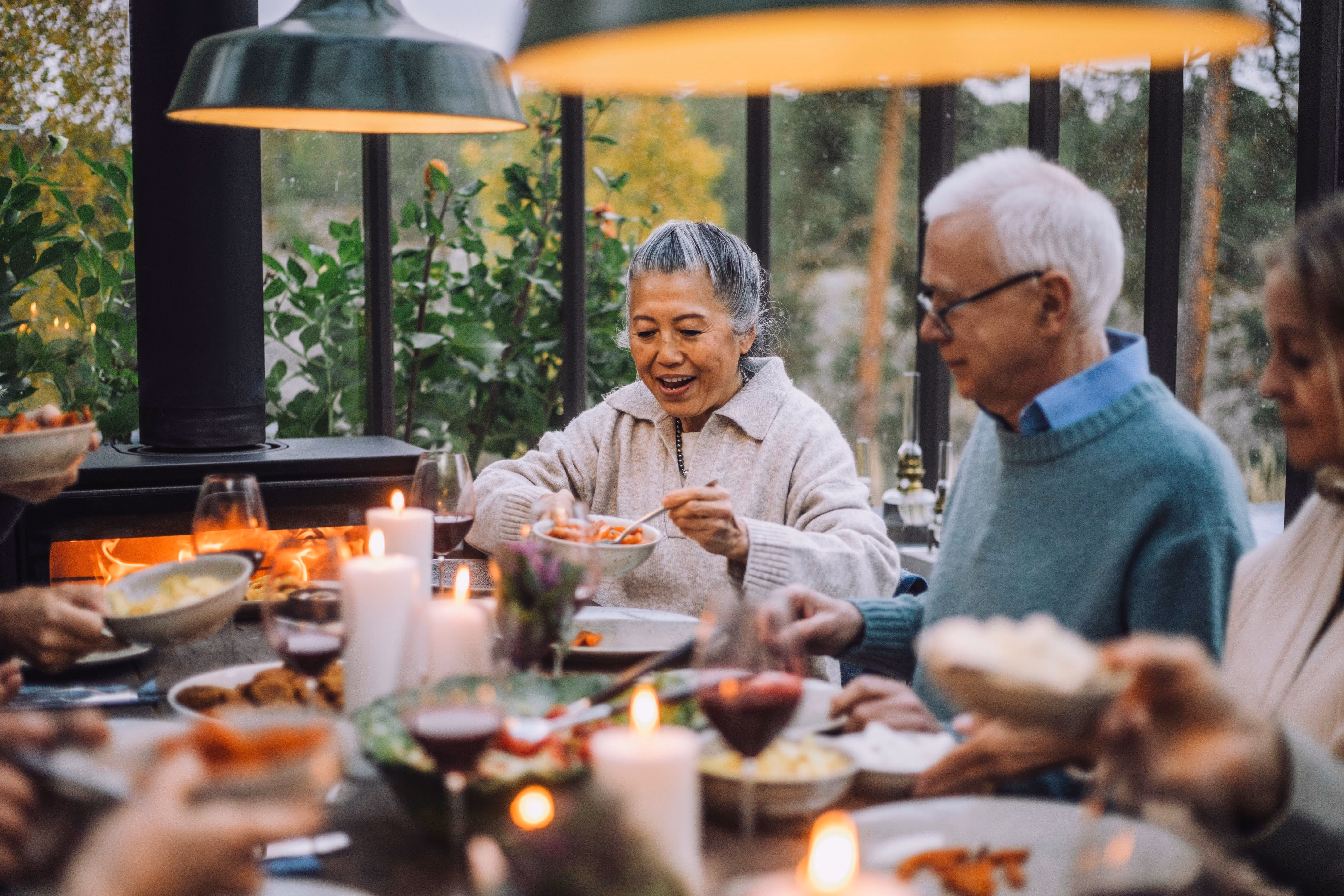 Älteres Paar teilt Dips und Gerichte an einem Abendessen bei Kerzenlicht mit Freunden im Freien [no AI]