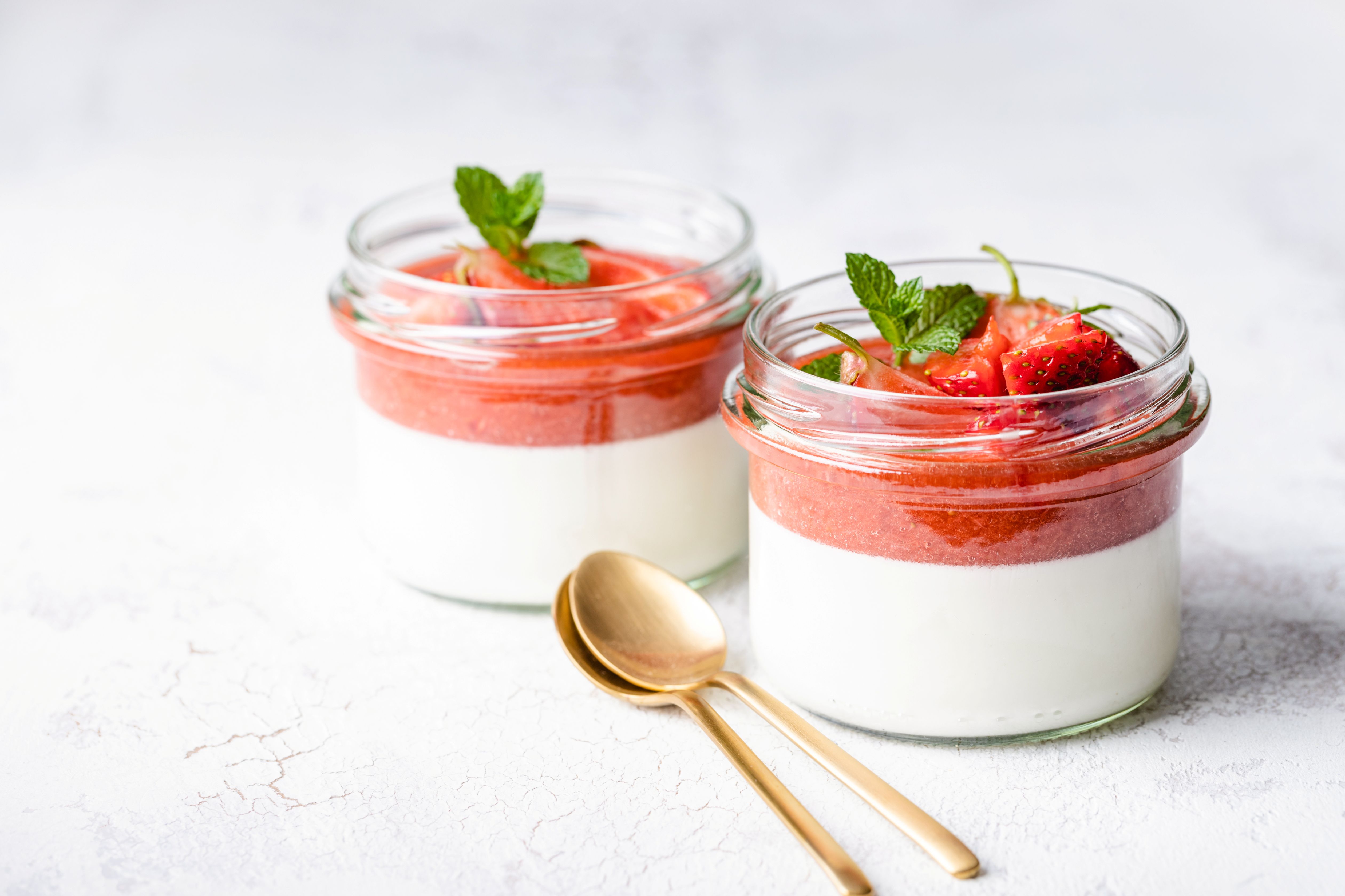 Two jars of layered strawberry panna cotta with mint and gold spoons