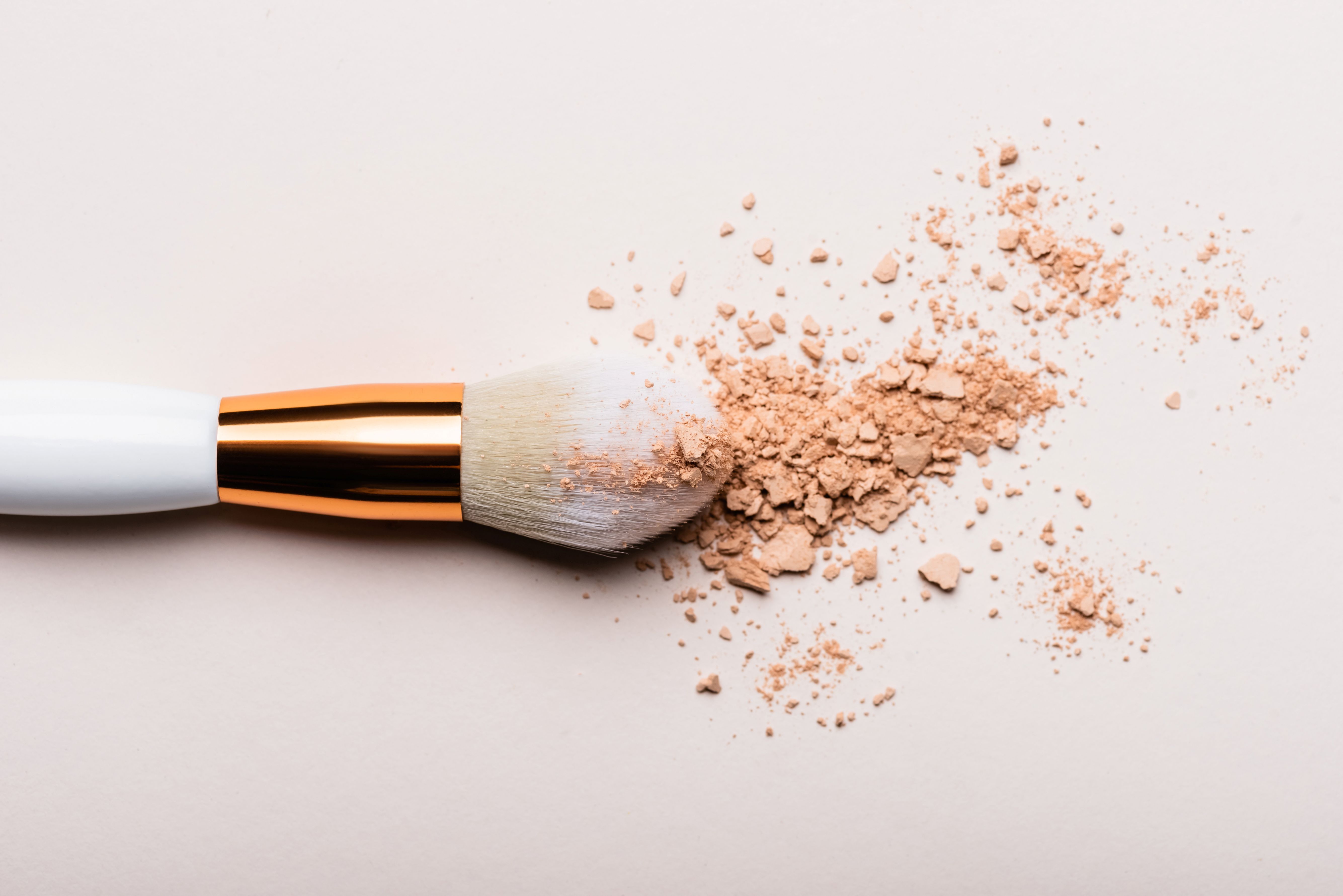 Make-up brush with crumbled beige powder on a light background