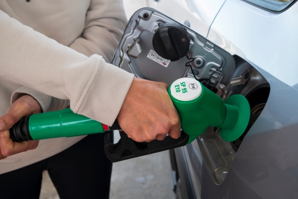 Hand hält eine grüne Zapfpistole mit Aufschrift SP95 E10 an den Tankstutzen eines Autos
